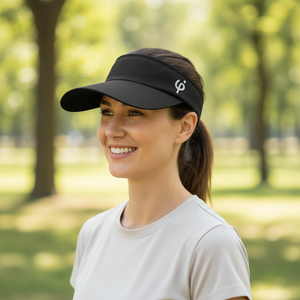 Mujer deportista sonriendo mientras usa una visera negra Frouros en un parque, protección solar con estilo para entrenamiento al aire libre.