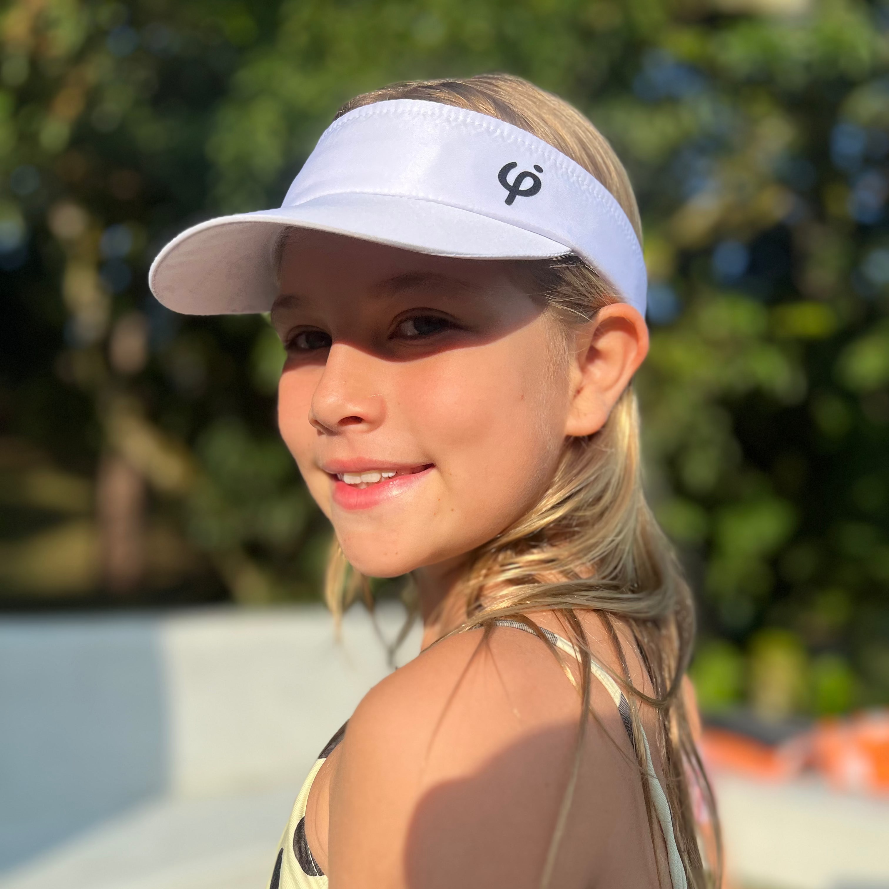 Niña deportista usando visera blanca Frouros de perfil, accesorio cómodo y ajustable para días de sol y entrenamiento.